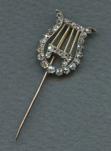 Image of a gold tie pin in the form of a four-stringed classical lyre, decorated with diamonds set in silver